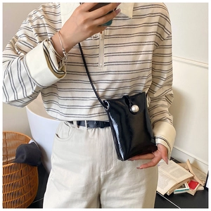 Detail of a mini black glossy shoulder bag with a prominent white pearl button closure