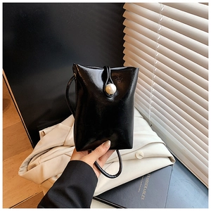 Detail of a mini black square crossbody bag featuring a large decorative white pearl clasp