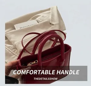 Close-up of red glossy patent leather handbag with gold zipper and dual handles