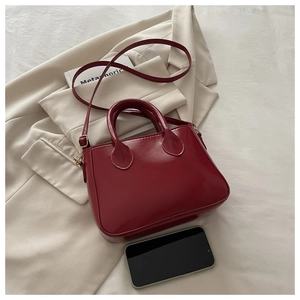 Red patent leather crossbody bag with dual handles shown next to a smartphone for size scale