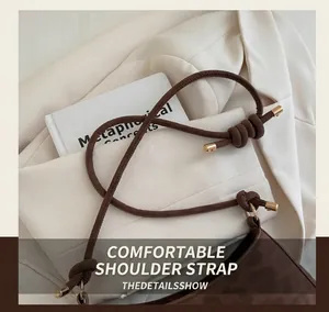 Detail of knotted shoulder strap on brown suede bag over a beige blazer