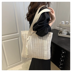 Close-up of a woven straw tote bag with fabric straps and white tassel decoration