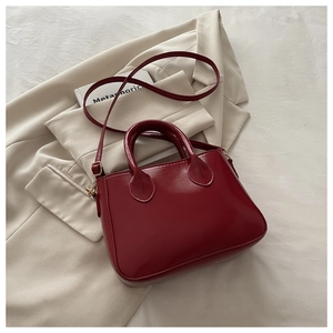 Close-up of glossy wine red crossbody bag with golden hardware on a beige blazer
