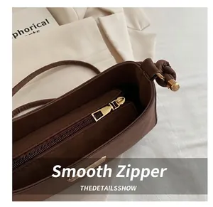 Detail of a dark brown shoulder bag featuring a smooth gold zipper and knotted strap design
