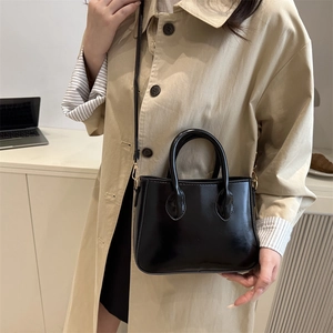 Classic black patent leather crossbody bag shown on a model with minimalist styling