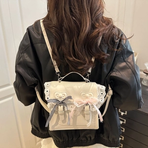 White mini lace backpack with bow detailing shown on a model in a black leather jacket