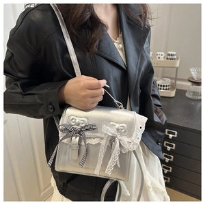 Detail of silver metallic crossbody bag with lace trim and bow on a model