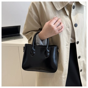 Detail of glossy black patent leather handbag styled with a beige trench coat and modern dress