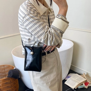 Mini black patent leather crossbody bag with pearl detail shown in a stylish indoor setting