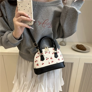 Mini shell handbag with cherry print, white and black leather, modeled on grey hoodie