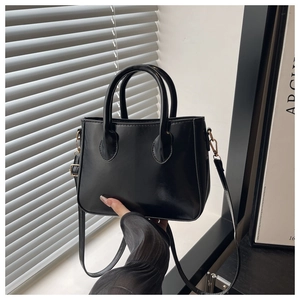 Close-up of minimalist black leather handbag showing smooth texture and golden metal hooks