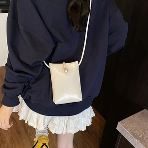 Sac à bandoulière blanc brillant avec boucle en perle porté par une femme mannequin