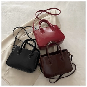 Three classic colors of glossy square handbags displayed on an elegant beige blazer