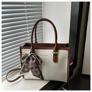 Detail of embossed tote bag with brown leather handles and a decorative silk scarf