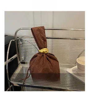 Détail du sac seau en daim marron avec boucle goutte dorée polie et texture douce au toucher