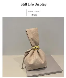 Détail du sac seau en daim kaki avec poignée dorée élégante posé sur des livres