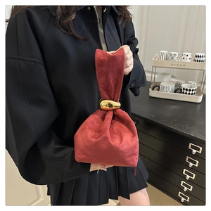 Détail d'un sac seau en daim rouge foncé avec boucle dorée et texture plissée