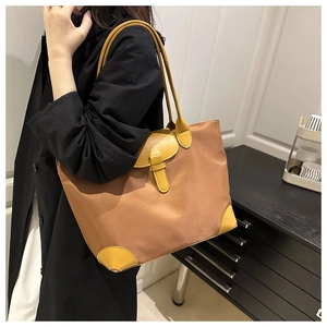 Detail of a large brown nylon tote bag with yellow leather accents on a female model