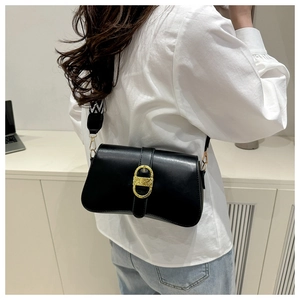 Close-up of black leather crossbody bag featuring a golden textured oval buckle and strap