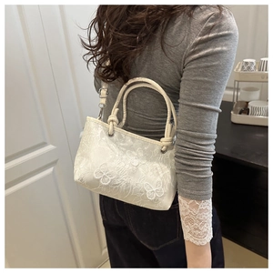 Detail of white butterfly embroidery and lace texture on a stylish square crossbody bag