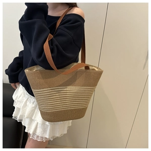 Detail of striped straw tote bag with brown shoulder straps worn by model for beach style