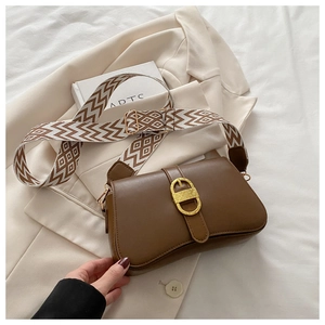 Close-up of brown leather crossbody bag with vintage gold buckle and woven strap