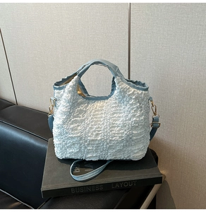 Détail de la texture gaufrée bleu clair et des ferrures dorées sur le sac à main