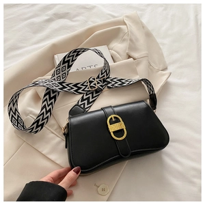 Close-up of a black leather bag with a gold D-buckle and striped shoulder strap