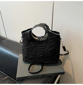 Close-up of black bubble textured crossbody bag with leather handle on a gray book