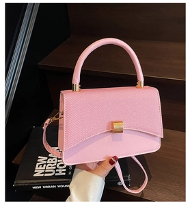 Detail of light pink square crossbody bag with gold buckle on wooden background