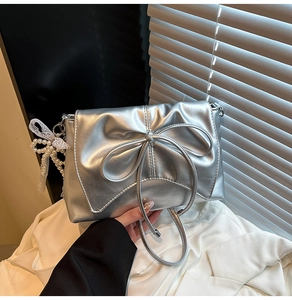 Détail du sac à bandoulière argenté métallisé avec nœud et breloque en perles et dentelle