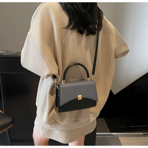Detail of grey fabric and black leather handbag with golden twist lock on a model
