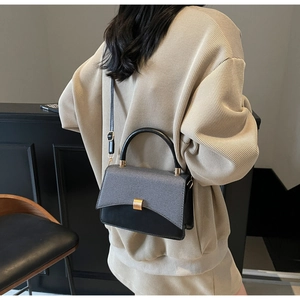 Détail du sac bandoulière bicolore gris et noir avec texture tressée et boucle dorée