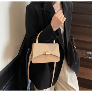 Close-up of elegant beige leather shoulder bag with gold clasp shown on a model