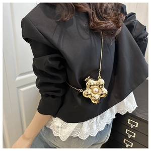 Detailed shot of golden flower acrylic mini bag with pearl center worn over a black blazer