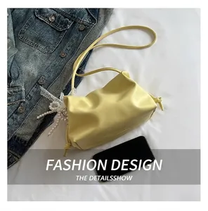 Detail of yellow pleated cloud bag with white lace and pearl charm on denim background