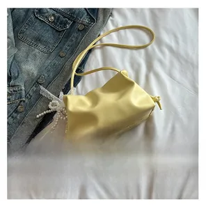 Detail of yellow pleated cloud bag with white lace and pearl charm on denim background