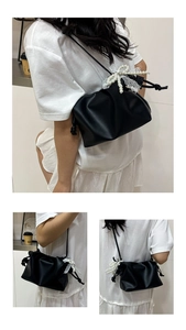 Detail of black pleated cloud bag featuring large white pearl and lace bow decoration