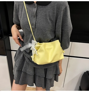 Detail view of yellow crossbody bucket bag with lace bow and pearl pendant charm