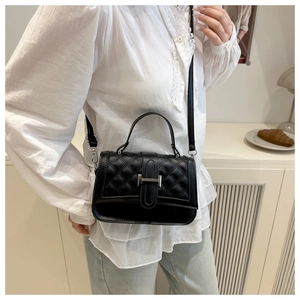 Detail view of a black quilted handbag featuring a silver H-shaped buckle on a model