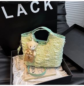 Détail du sac à main vert clair en tissu gaufré avec un pendentif ours dans une boîte cadeau