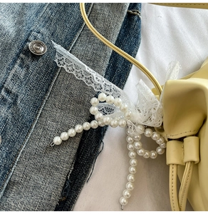 Detail of light yellow leather bucket bag with pearl lace bow and pleated edge texture