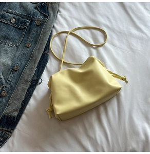 Detail of light yellow ruched bucket bag with drawstring knot on a white background