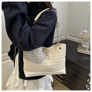 Detail of a straw tote bag featuring chain straps and a golden deer charm accent