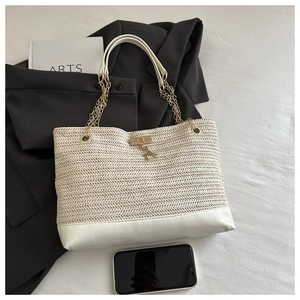 Detail of woven straw tote bag with gold chain handle and white leather trim accents