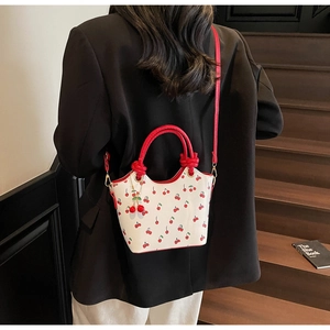 Détail du sac à main blanc à motif cerise avec poignée tressée rouge porté par mannequin