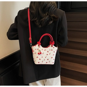 Détail d'un sac seau à imprimé cerise avec poignées rouges et breloque sur un modèle