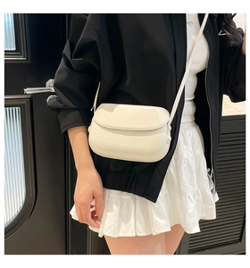 Detail of a creamy white saddle bag worn with a black jacket and white pleated skirt