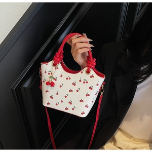 Détail d'un sac seau blanc à imprimé cerises avec poignées rouges et breloque cerise