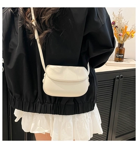Detail of cream saddle bag with adjustable strap and flap closure worn over the shoulder